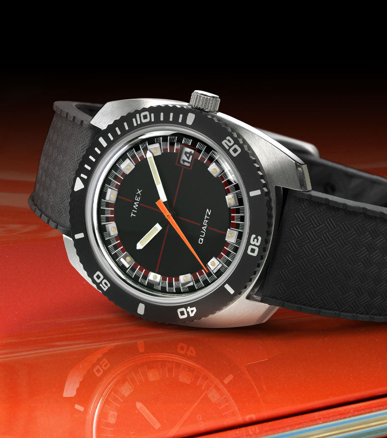 Q Timex Reissue sitting atop a red car hood with a reflection of the watch in the forefront