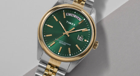 Stainless steel and gold coloured watch with green dial on a grey background.