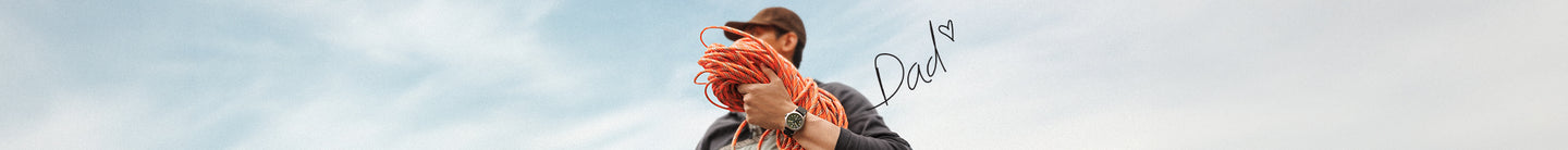 Father’s Day featuring a man outdoors holding a coil of orange climbing rope while wearing a wristwatch. The background shows a cloudy sky, with the handwritten word ‘Dad’ and a small heart graphic adding a personal, heartfelt touch.