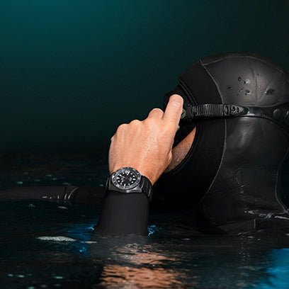 A diver wearing a black wetsuit adjusts their mask at the water's surface, showcasing the Timex Deepwater watch on their wrist. The scene captures the moment before submersion, emphasizing readiness and reliability.