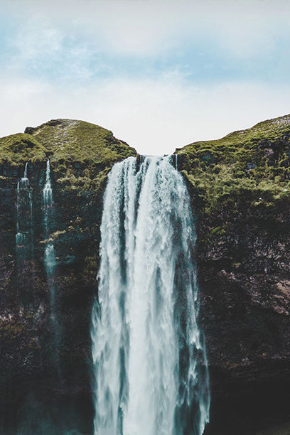Tall waterfall cascading down a rocky cliff with greenery on either side.