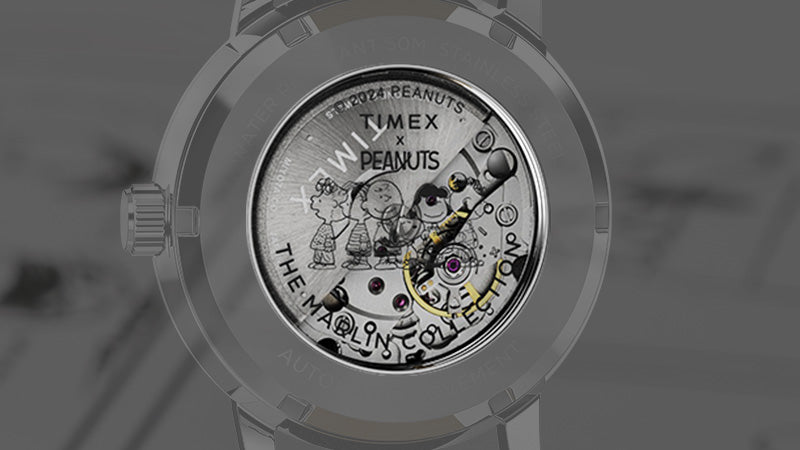 The exhibition caseback of the Timex Marlin® Automatic reveals a mechanical movement adorned with printed artwork of Peanuts characters, including Charlie Brown, Lucy, and Snoopy. Text reads “Timex x Peanuts” and “The Marlin Collection.”