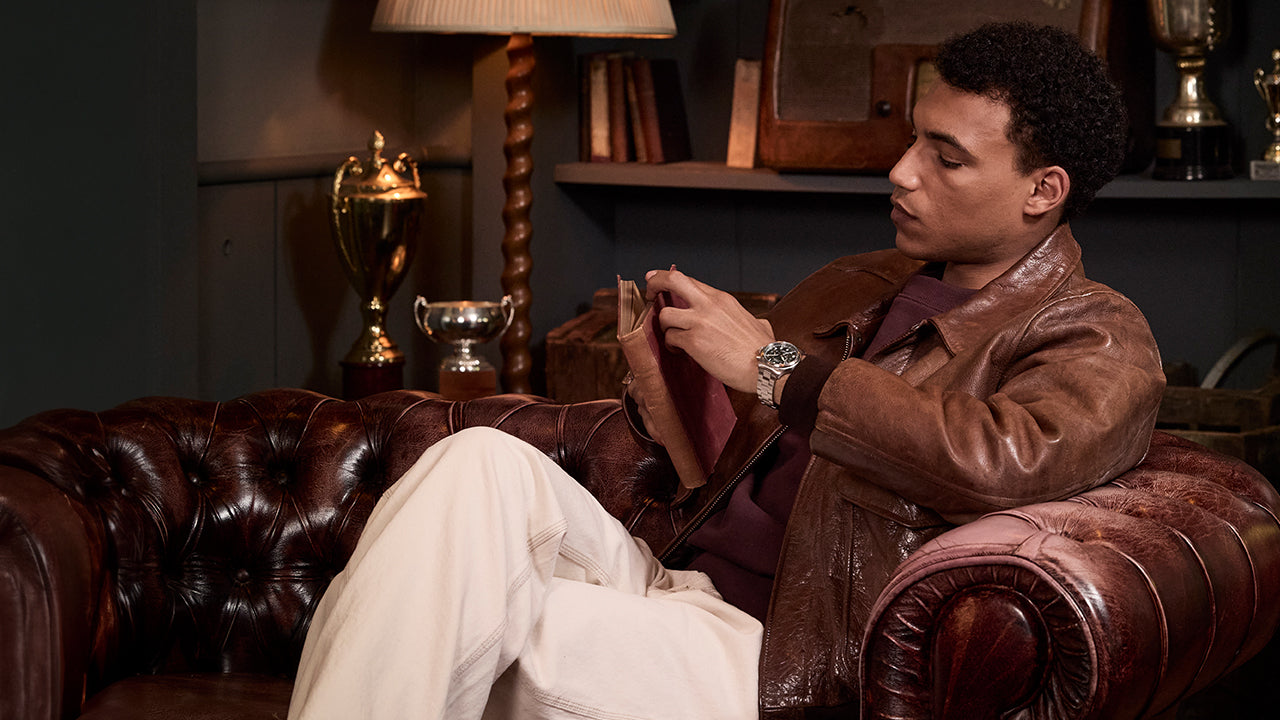 Man sitting on a leather armchair reading a book, wearing the Timex Waterbury Ace Chronograph with stainless steel bracelet and green dial.
