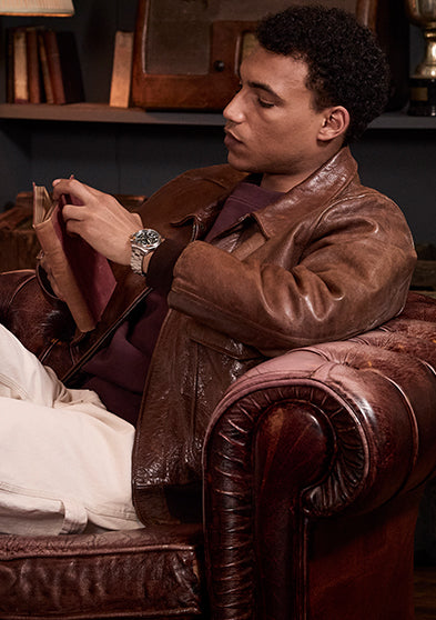 Man sitting on a leather armchair reading a book, wearing the Timex Waterbury Ace Chronograph with stainless steel bracelet and green dial.