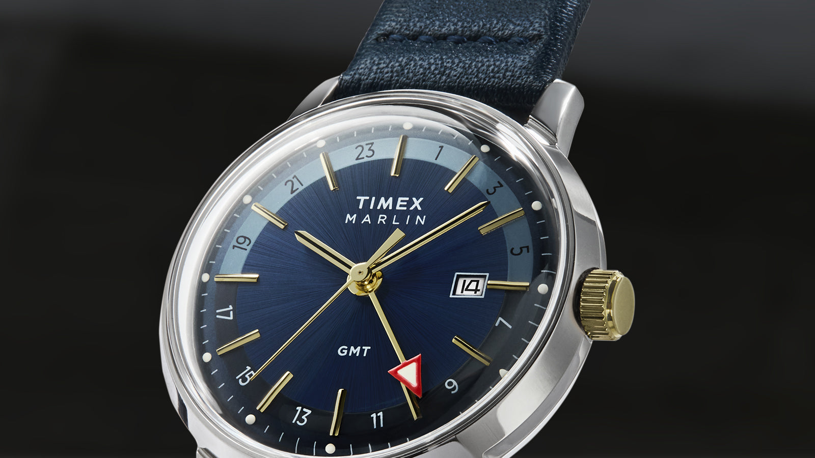 A detail-focused image of the Timex Marlin® Quartz GMT’s navy dial with gold accents, red GMT hand, and gold-tone crown. The brushed finish on the dial adds depth to the design.