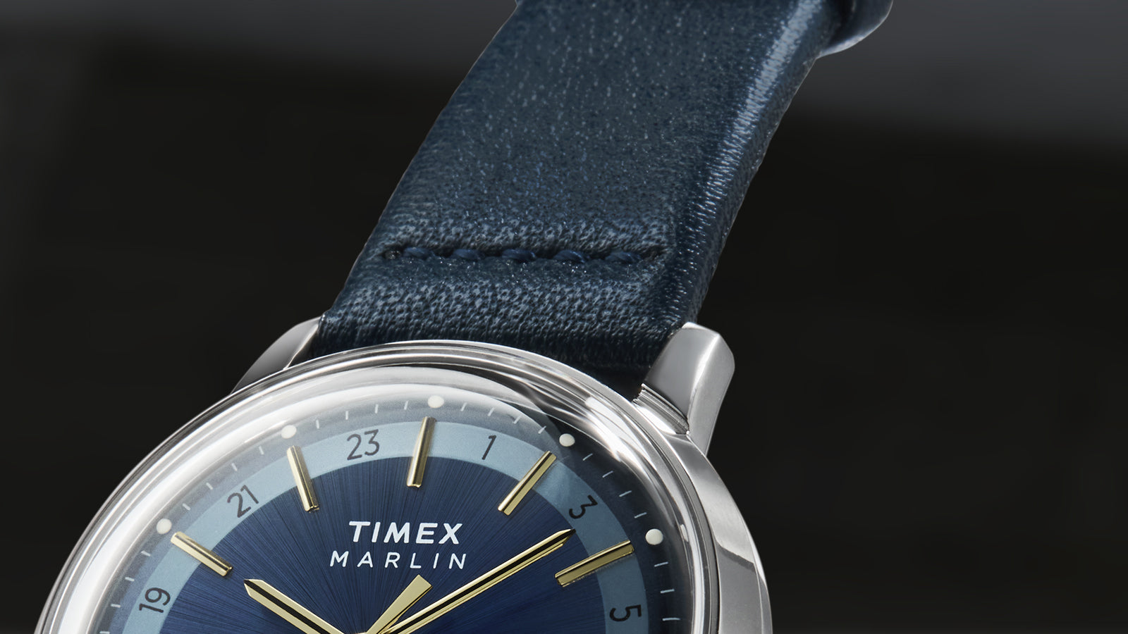 A close-up of the navy leather strap and top section of the Timex Marlin® Quartz GMT. The stitching and texture of the strap are visible, with the polished case and markers providing contrast.