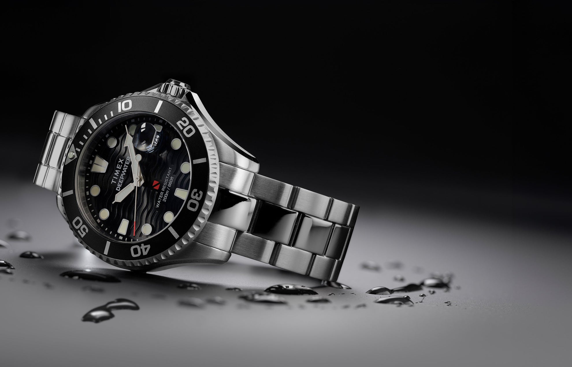 Timex Deepwater Meridian 200 dive watch in stainless steel with black rotating bezel and wavy black dial, lying at an angle with water droplets on the surface.