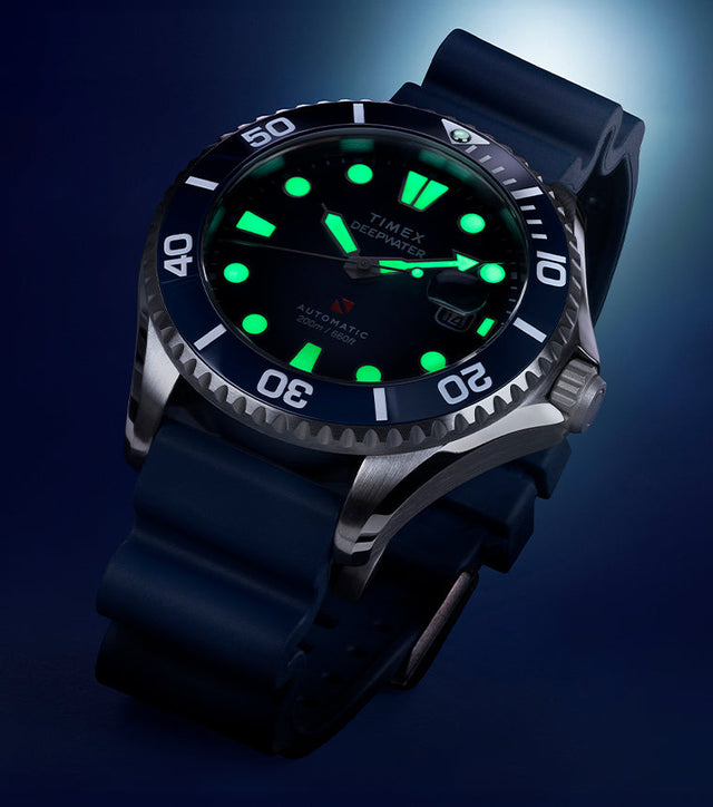Close-up of the Timex Deepwater Meridian 200 automatic dive watch with luminous markers glowing green against a dark blue background.