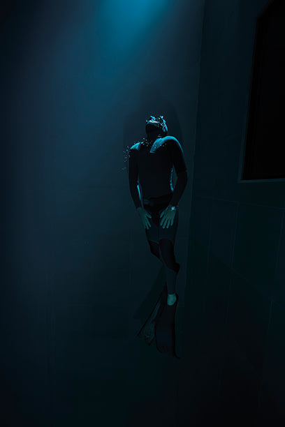 Freediver in a wetsuit illuminated by a beam of light underwater, wearing the Timex Deepwater Meridian 200 dive watch while floating upward in the deep.
