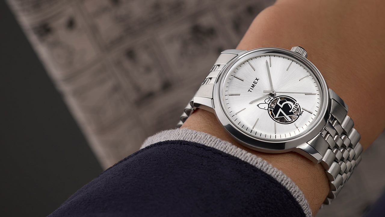 Timex x Peanuts® Marlin® Automatic watch on a wrist, featuring a silver-tone dial with Snoopy sitting atop a black-and-white 75 Years logo at the 6 o’clock position, silver indices, and stainless steel bracelet.