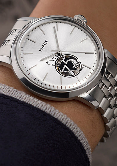 Timex x Peanuts® Marlin® Automatic watch on a wrist, featuring a silver-tone dial with Snoopy sitting atop a black-and-white 75 Years logo at the 6 o’clock position, silver indices, and stainless steel bracelet.