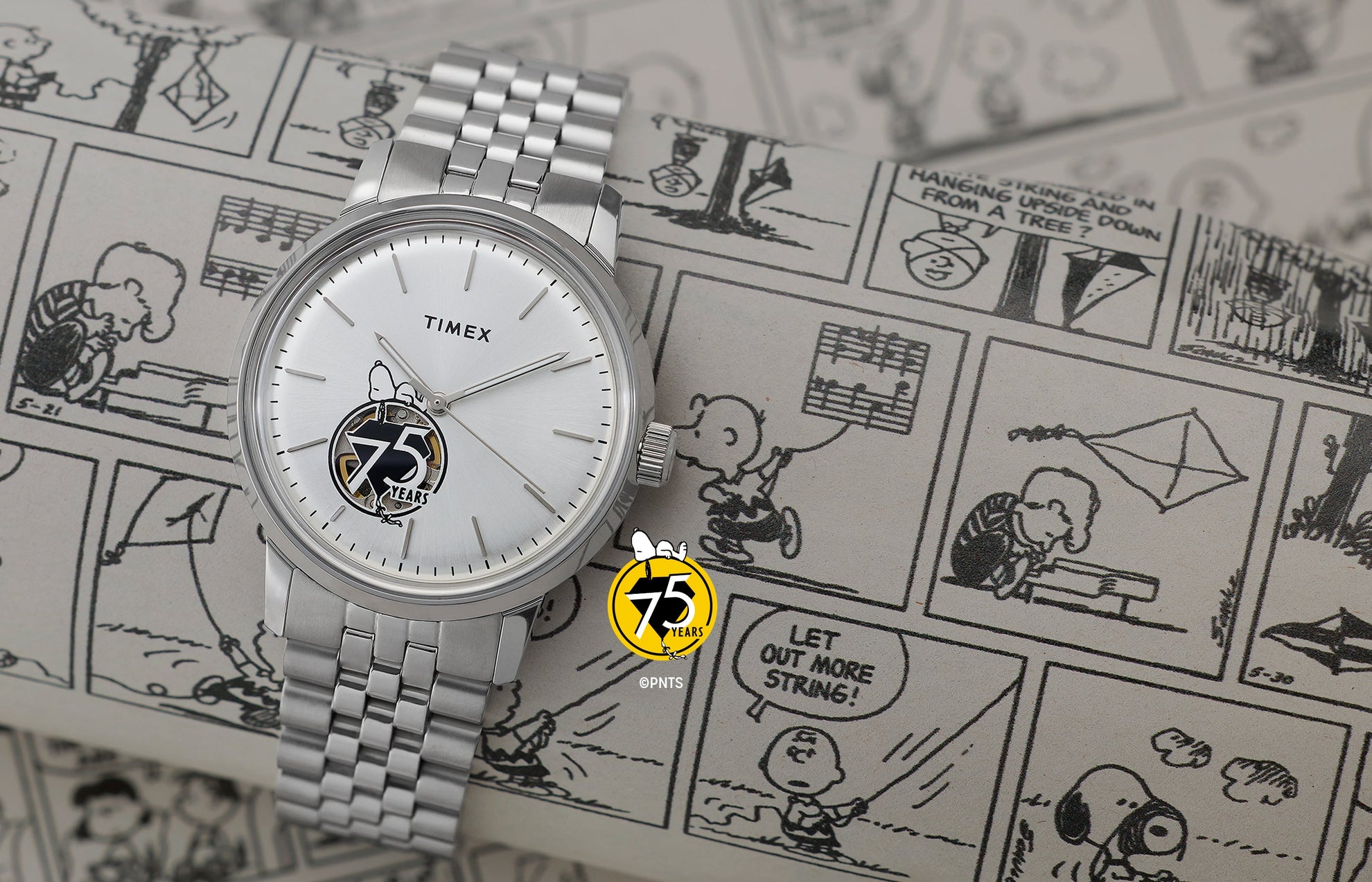 Timex x Peanuts® Marlin® Automatic watch placed over black-and-white Peanuts® comic strips, showing its silver-tone dial, minimalist indices, Snoopy illustration above the 75 Years logo, and open-heart movement view.