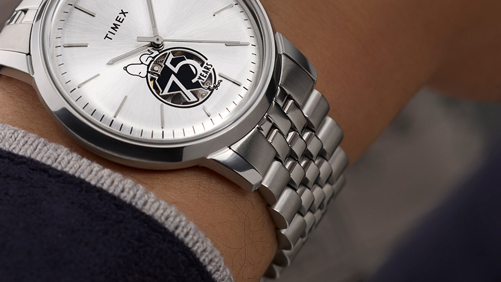 Angled close-up of the Timex x Peanuts® Marlin® Automatic watch on a wrist, showing brushed and polished stainless steel bracelet links and silver-tone dial with Snoopy 75 Years open-heart design.