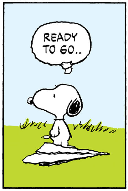 Snoopy sits on a blanket on the grass with a determined expression, thinking the words “READY TO GO..” in a speech bubble.