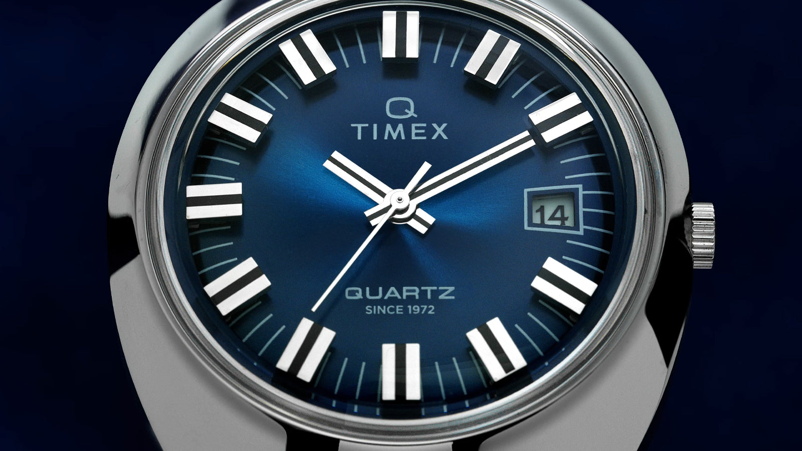 Close-up of the Q Timex® 1972 Time Machine Reissue dial showcasing the rich blue sunray finish, bold silver-tone hour markers with black accents, luminous hands, and a framed date window at 3 o’clock, with “Q Timex” and “Quartz Since 1972” printed on the dial.