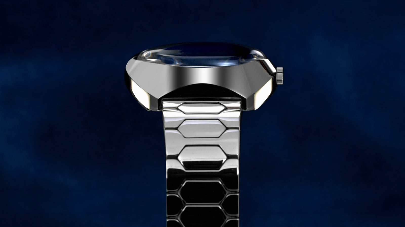 Top-down view of the Q Timex® 1972 Time Machine Reissue highlighting its polished stainless-steel case, faceted edges, domed crystal, and hexagonal-link bracelet, set against a dark blue gradient background.