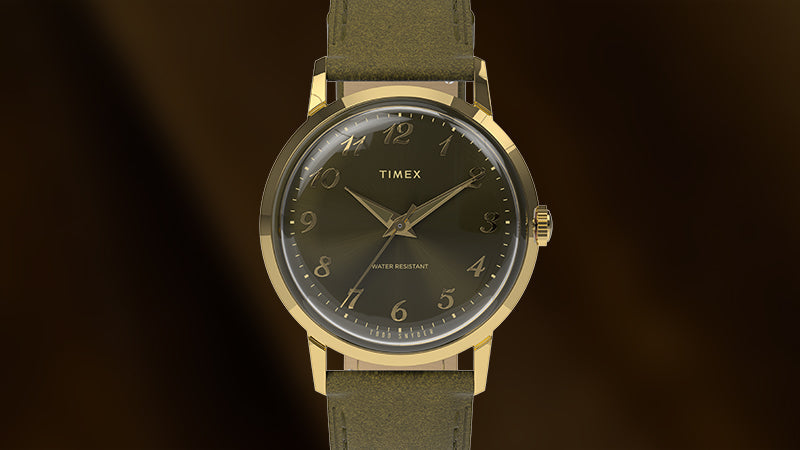 Front-facing product shot of the Timex x Todd Snyder watch against a dark brown background, highlighting its green dial, gold-tone case, and olive leather strap.