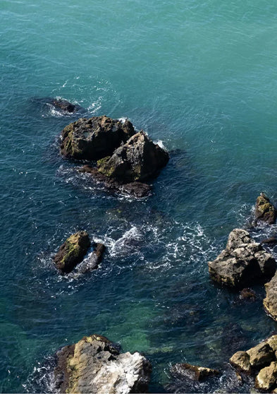 Aerial view of rocky shoreline with ocean waves splashing against the rocks, symbolizing outdoor adventure.