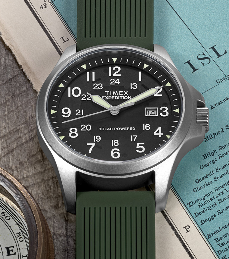 A Timex Expedition® Field Post Solar watch with green strap rests on an old map, paired with a compass, symbolizing exploration.