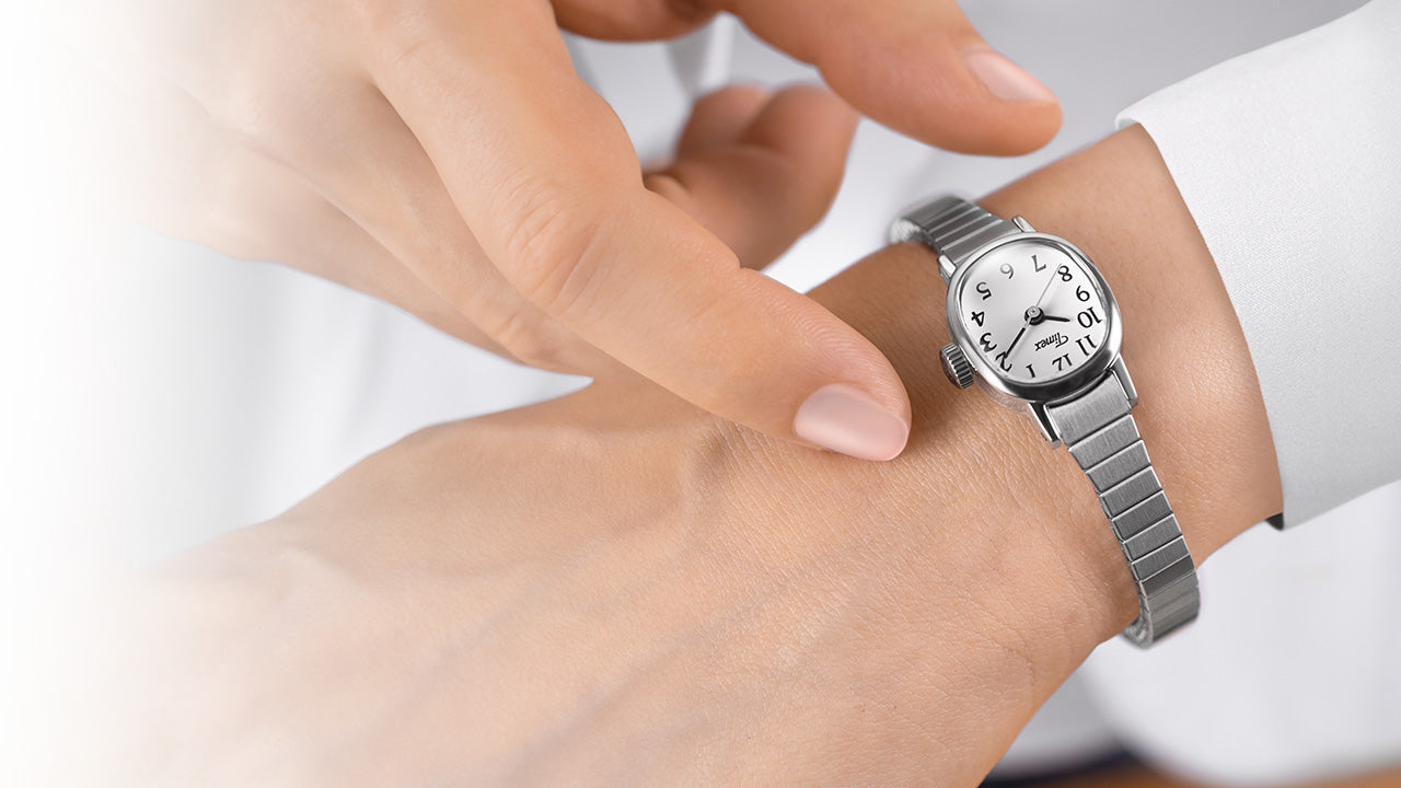Close-up of a Timex Cavatina Mini watch with silver-tone expansion band and white dial on a wrist, with a hand adjusting it.