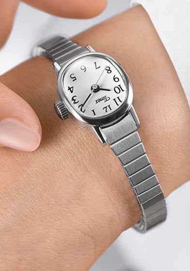 Close-up of a Timex Cavatina Mini watch with silver-tone expansion band and white dial on a wrist, with a hand adjusting it.