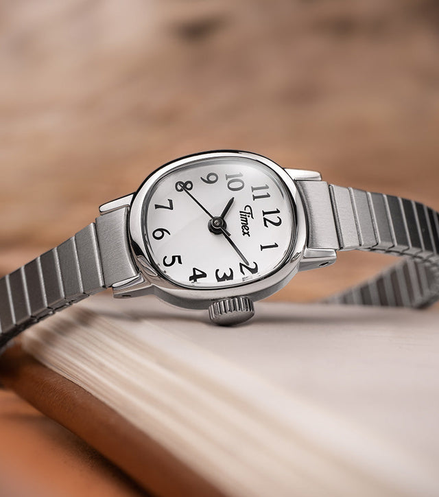 Timex Cavatina Mini watch with a silver expansion bracelet and white dial resting elegantly on the edge of an open book.