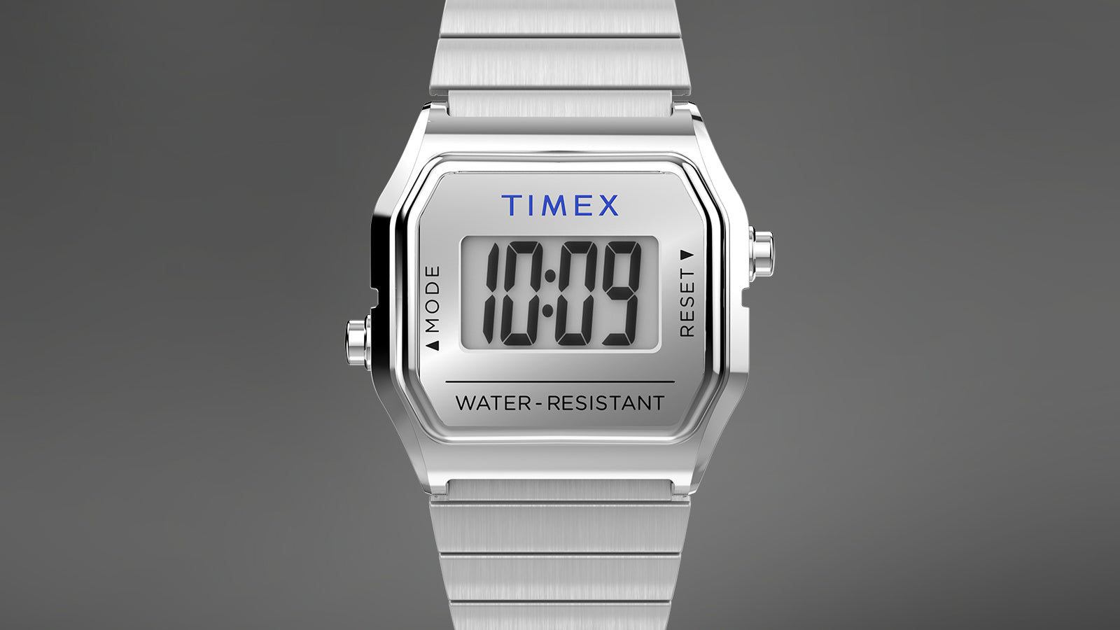 Front view of the Teeny Tiny Timex digital watch displaying the time “10:09” on a clear digital screen with “TIMEX” branding above and “WATER-RESISTANT” text below. The compact silver-tone case and bracelet evoke a classic 1980s retro style.