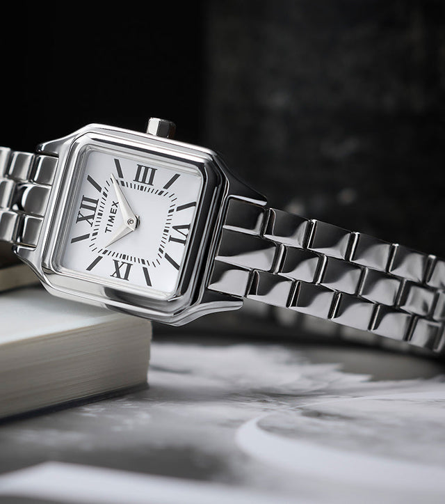 Timex Legacy Addison silver-tone women’s watch with square, rounded-corner case, white dial with black Roman numerals, and polished link bracelet, styled on books.