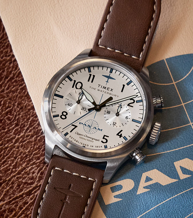Close-up of the Timex x Pan Am® Waterbury Ace Chronograph with a white dial, black numerals, and brown leather strap resting on vintage Pan Am travel documents.