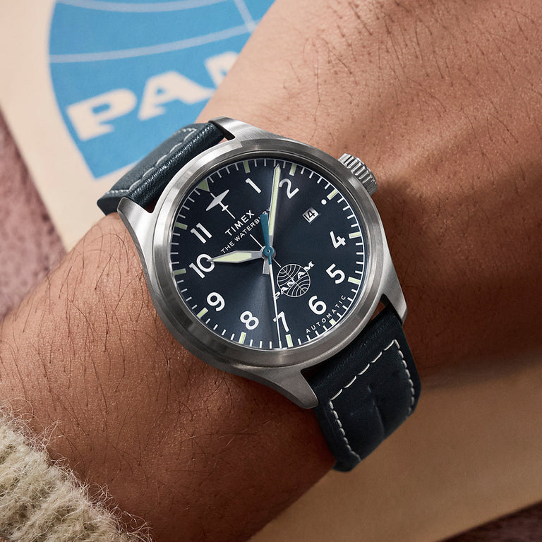 Timex x Pan Am® Waterbury Ace automatic watch on wrist, showcasing the navy dial, white Arabic numerals, date window, and Pan Am globe logo above 6 o’clock.