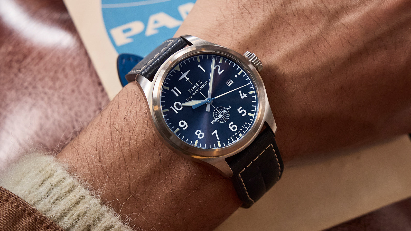 Wrist shot of the Timex x Pan Am® Waterbury Ace with navy dial, date display at 3 o’clock, luminous hands, and vintage-inspired aviation design.