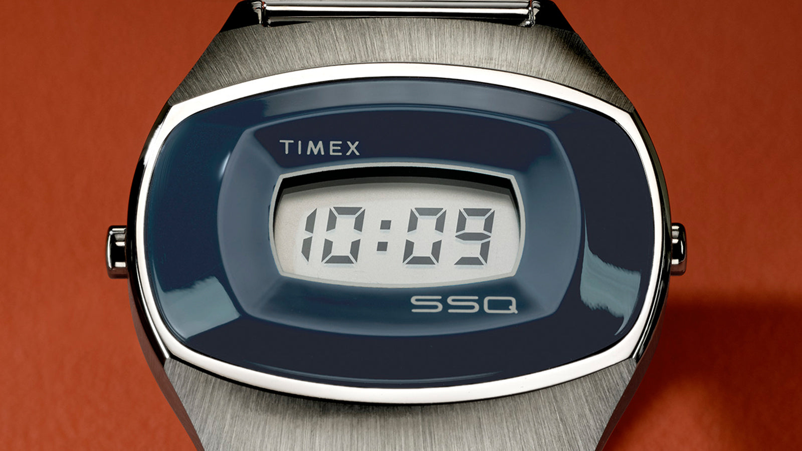 Detailed front view of the Q Timex® 1975 SSQ Digital Reissue showing its curved oval blue bezel, stainless-steel case, and minimalist digital display reading “10:09.”