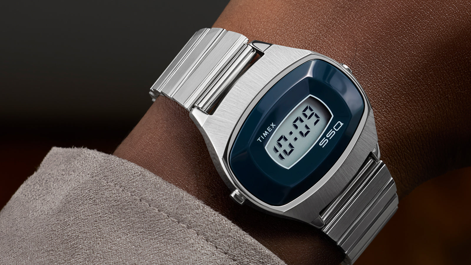 Q Timex® 1975 SSQ Digital Reissue on wrist, featuring a polished stainless-steel bracelet and dark blue digital dial, photographed close-up with soft suede sleeve visible.