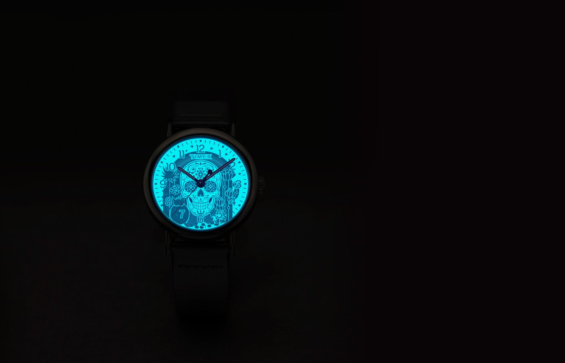 Timex Weekender Day of the Dead watch dial glowing in the dark with INDIGLO® backlight, revealing a bright blue sugar skull and floral details.