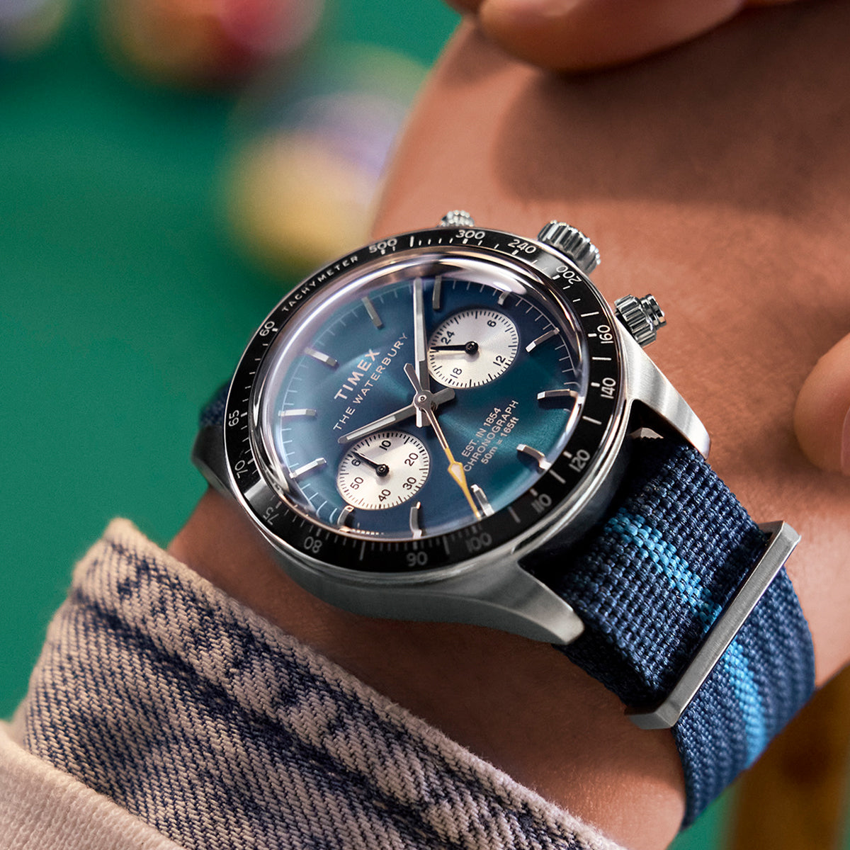 Timex Waterbury Heritage Chronograph with a blue dial and fabric strap, worn on wrist, showing silver subdials and yellow seconds hand.