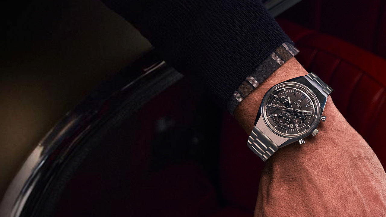 Person wearing the Q Timex Falcon Eye Chronograph while resting their arm in a vintage car interior with red leather seats, emphasizing the classic design.