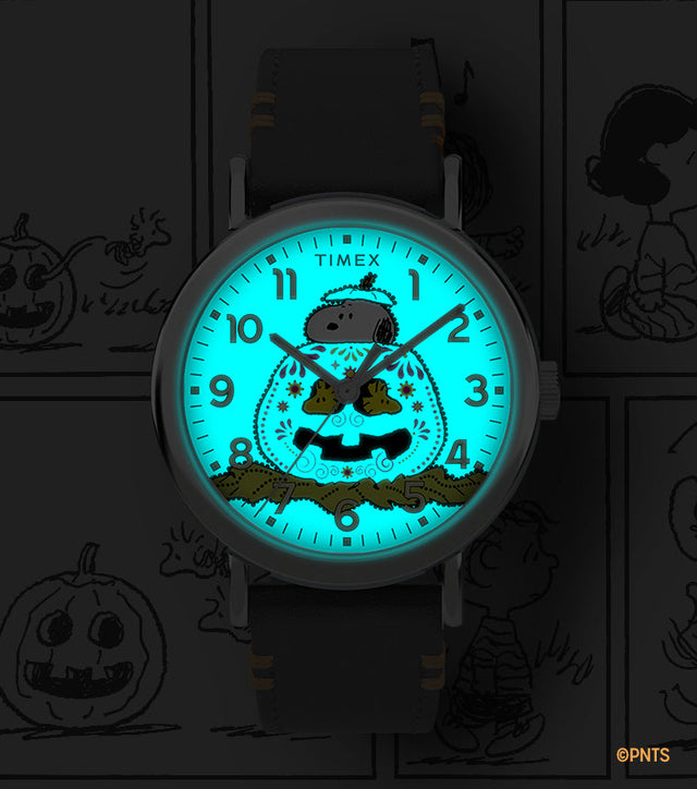 Timex x Peanuts® Weekender Pumpkin Dial watch glowing with INDIGLO® backlight, showing Snoopy and pumpkin design illuminated in bright blue.