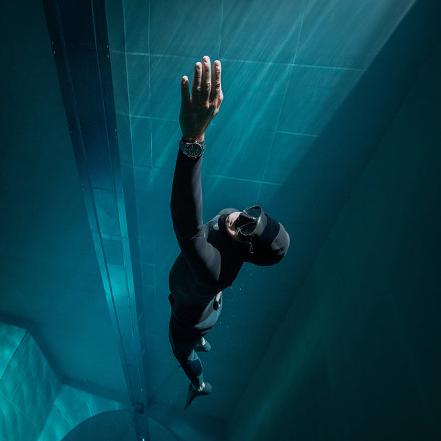 Underwater photograph of a diver wearing the Timex Deepwater watch while swimming upward toward the surface, illuminated by beams of light filtering through the water.