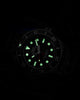 Timex Deepwater dive watch glowing in the dark, showing bright green luminescent hour markers and hands against the black dial, with the red seconds hand and bezel numerals faintly visible.