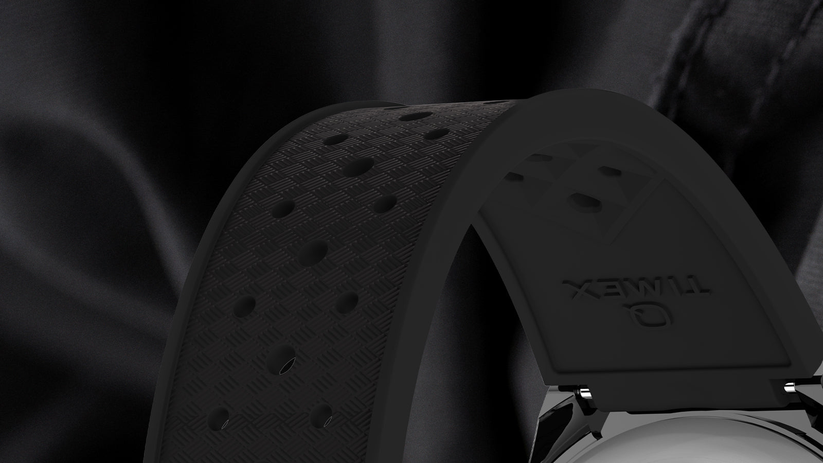 Close-up of the Q Timex GMT black rubber strap, showing textured perforations and embossed Timex branding on the underside for breathability and comfort.