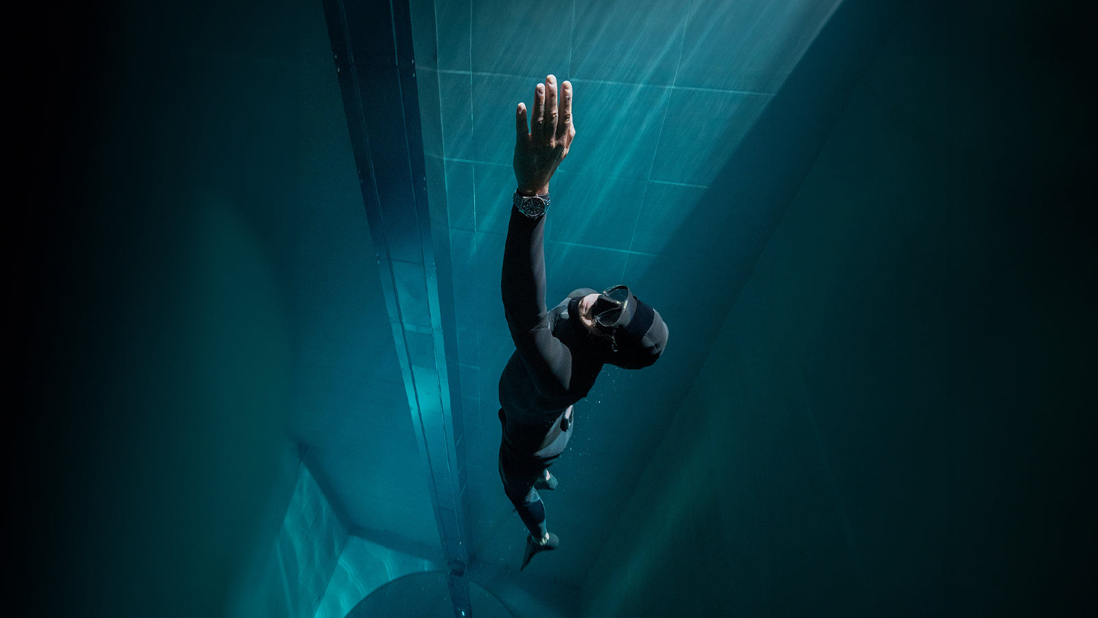 Underwater photograph of a diver wearing the Timex Deepwater watch while swimming upward toward the surface, illuminated by beams of light filtering through the water.