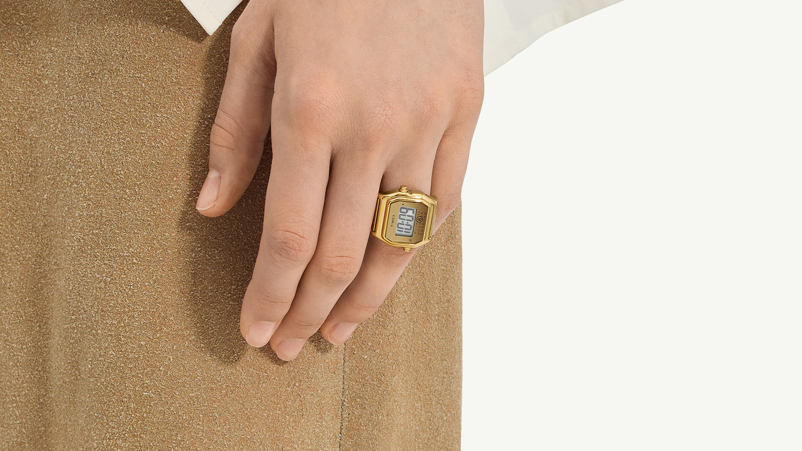 Detailed close-up of the Timex x MM6 T80 gold-tone digital display face, showing the Timex logo, retro calendar layout, and minimalist dual-button design on either side of the case.