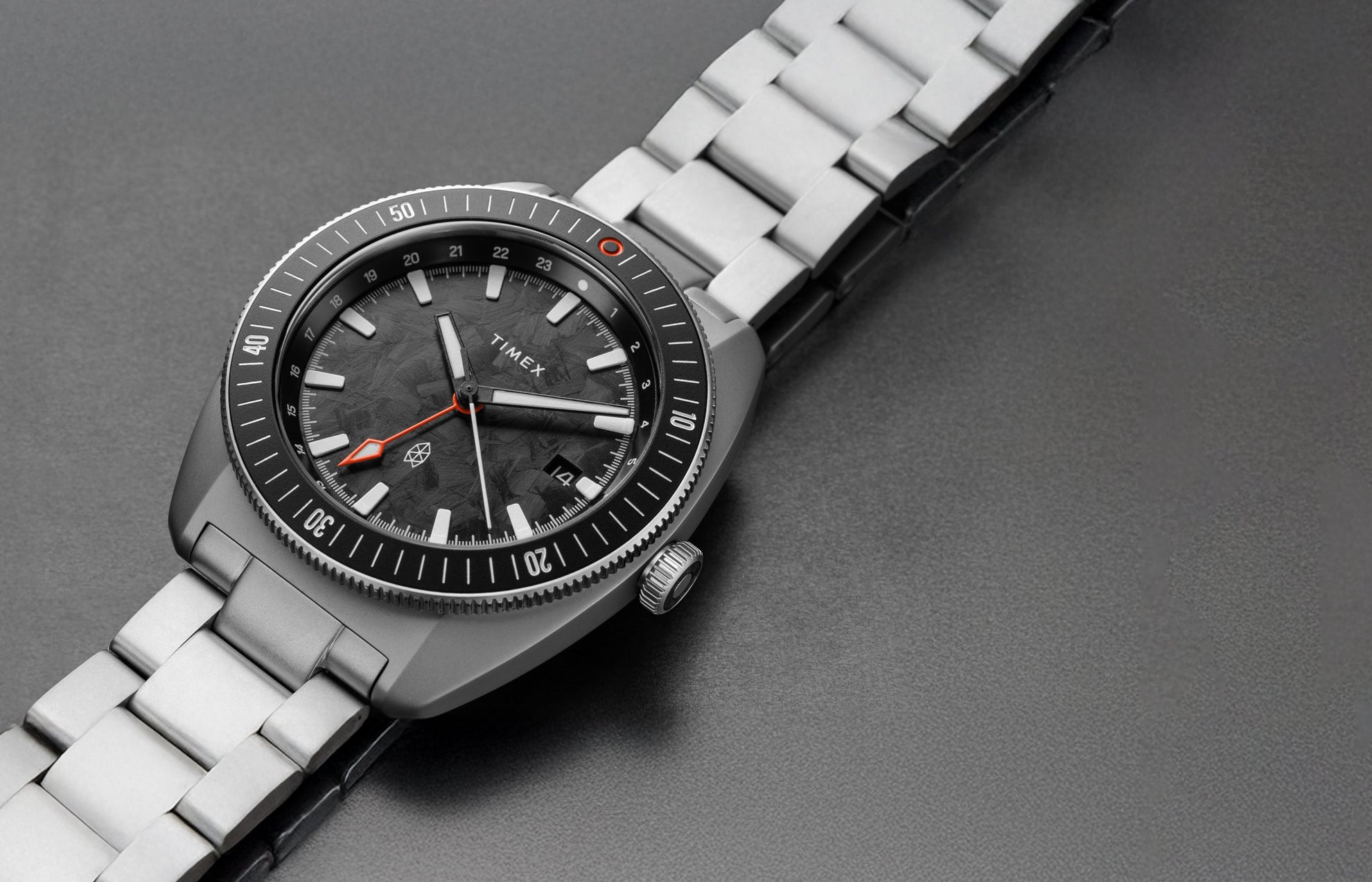 Close-up view of The James Brand x Timex GMT watch showing the black marbled dial, orange GMT hand, and stainless steel bracelet.