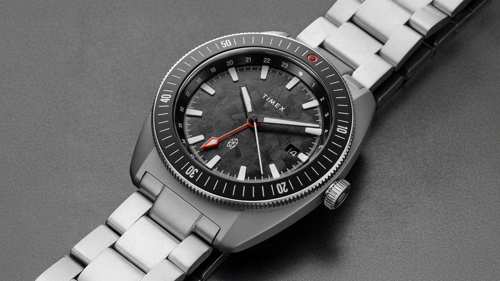 Close-up view of The James Brand x Timex GMT watch showing the black marbled dial, orange GMT hand, and stainless steel bracelet.