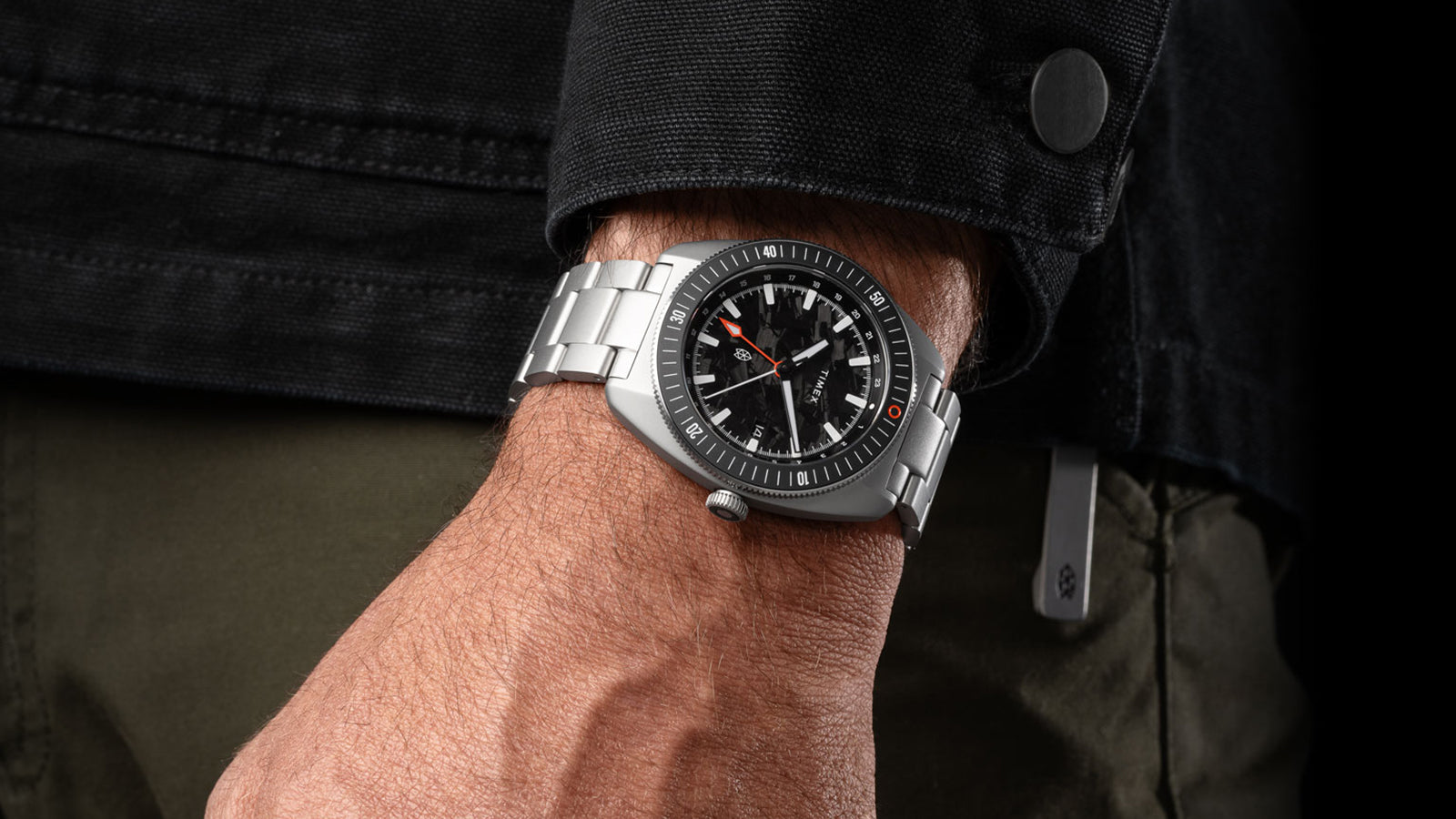 The James Brand x Timex GMT watch styled with a black jacket, highlighting its brushed steel case and bold design.