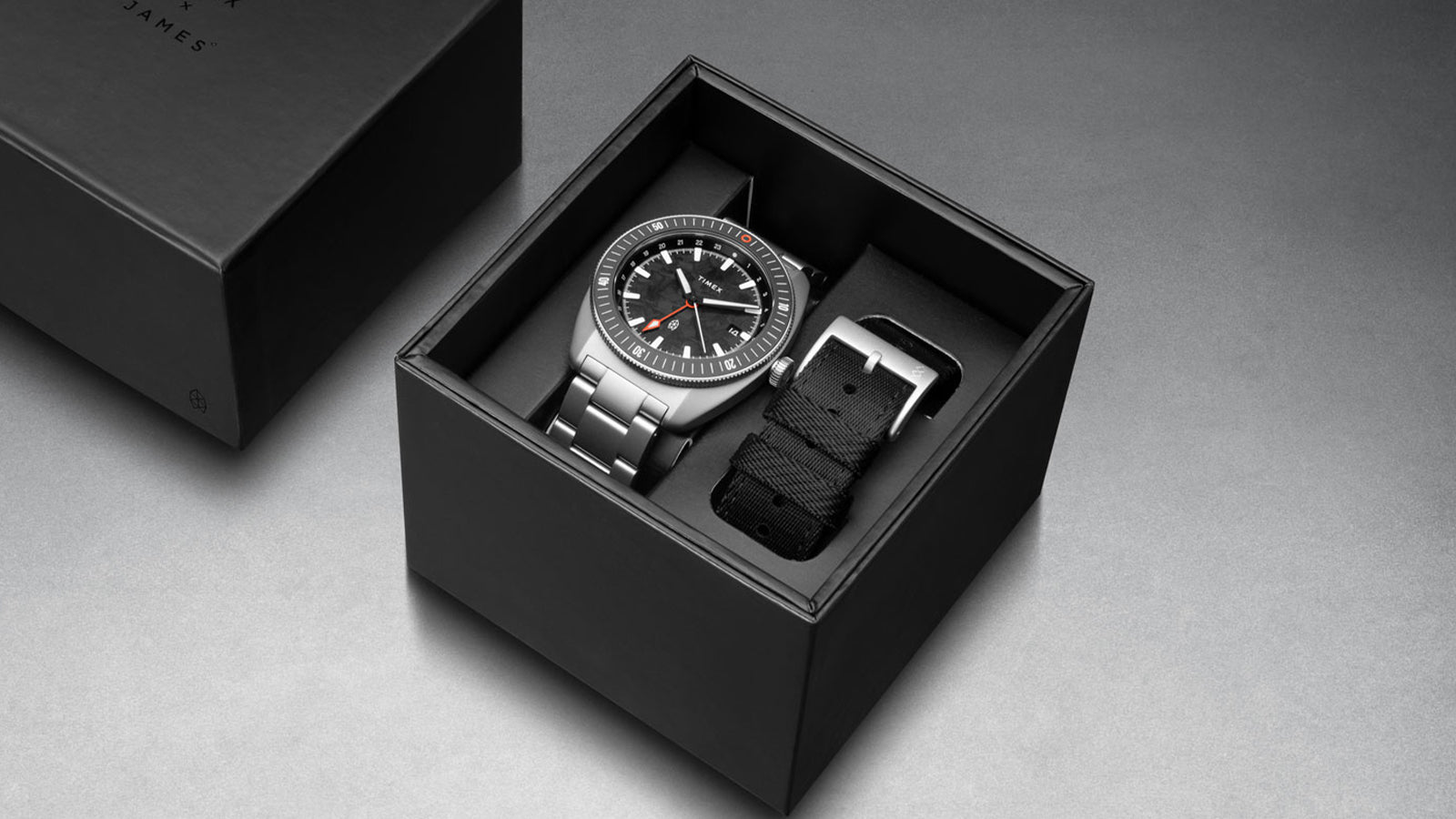 The James Brand x Timex GMT watch in black presentation box with additional black fabric strap, showcasing premium packaging.