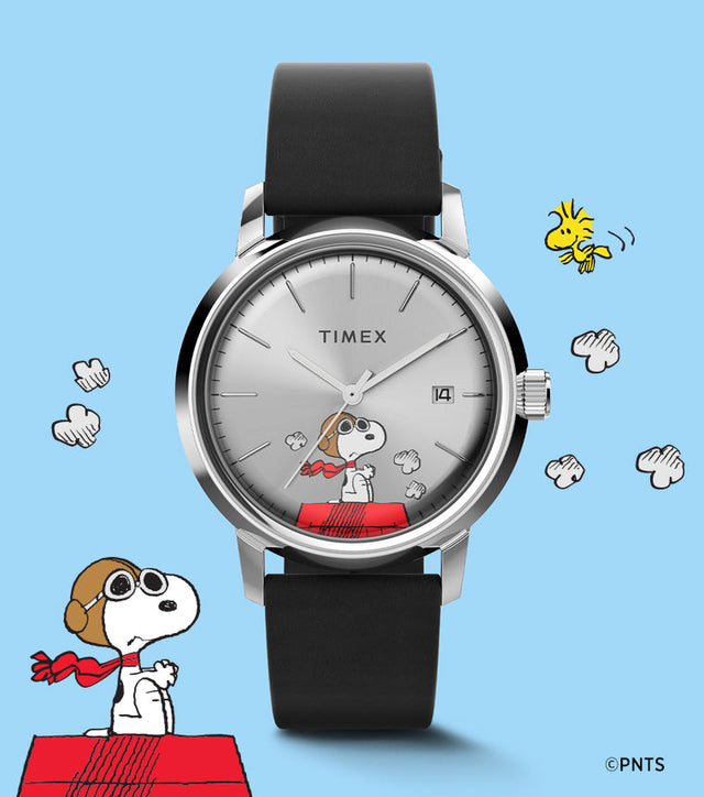 A Timex Marlin® Automatic x Peanuts Snoopy Flying Ace watch with a silver-tone dial and black leather strap displayed against a light blue background. Snoopy, dressed as a flying ace, sits on his red doghouse with clouds and Woodstock flying nearby, evoking a playful aviation theme.