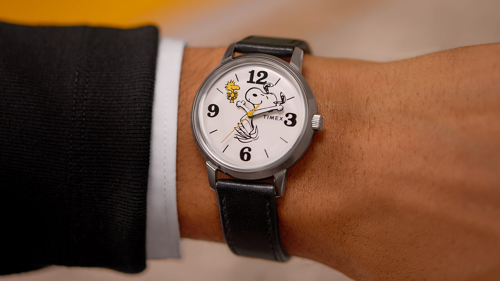 The Timex x Peanuts® Marlin® 75th Anniversary Edition watch worn on a wrist, showcasing Snoopy mid-swing and Woodstock on the white dial. The polished silver-tone case and black leather strap lend a refined, vintage appeal.