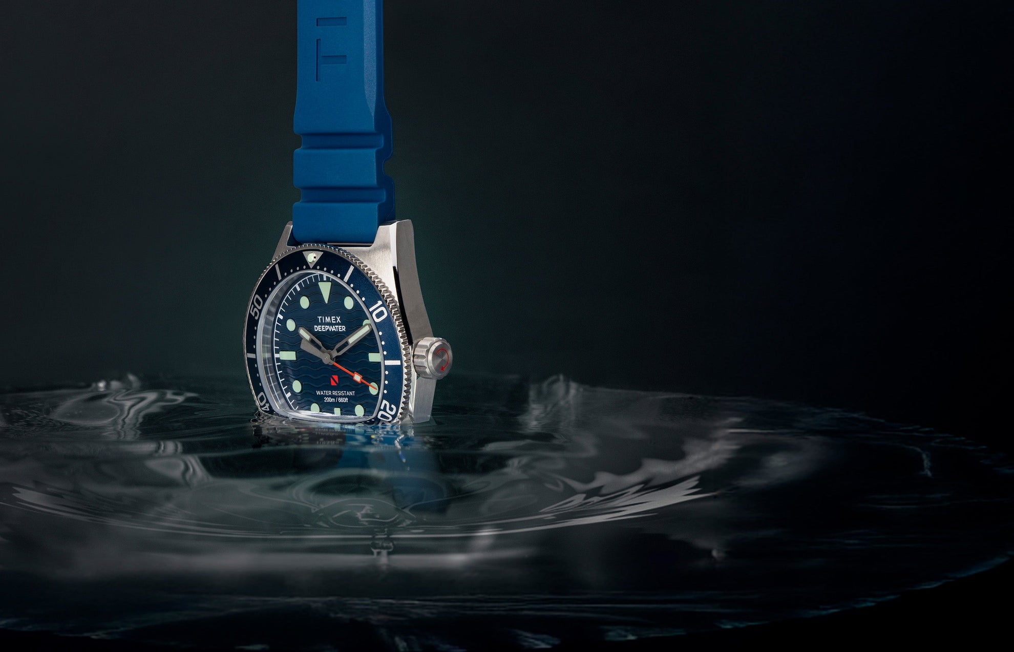 Timex Deepwater Reef 200 watch with blue dial and matching blue rubber strap, half-submerged in rippling water against a dark background, highlighting its aquatic performance design.