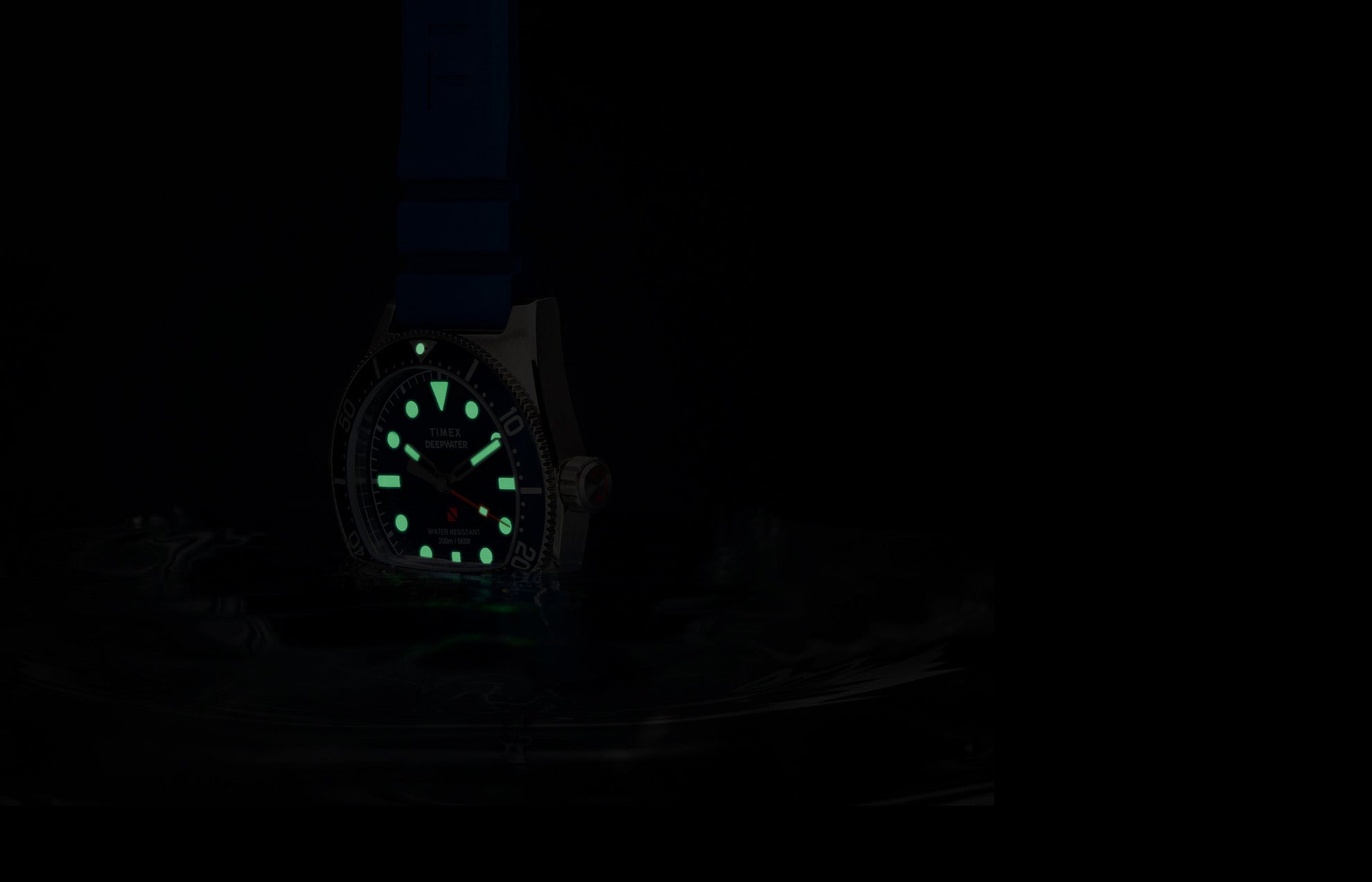 Timex Deepwater Reef 200 watch glowing underwater, with luminous markers and hands shining green in low light, emphasizing dive-ready legibility.